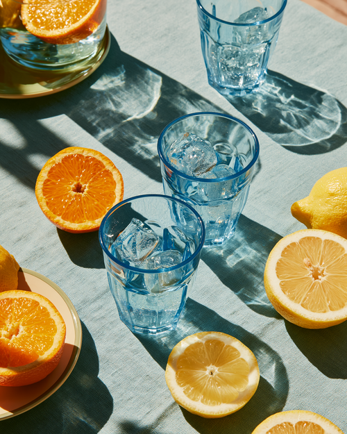 Blue glasses with ice and lemon slices on a gray surface with oranges and lemons.