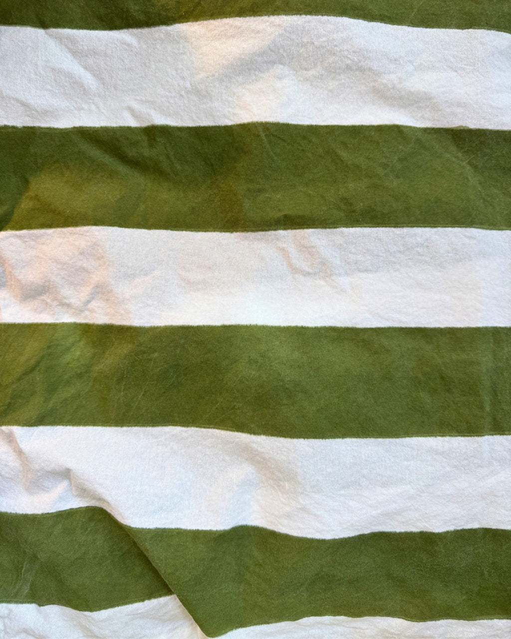 A close-up of a striped fabric with alternating horizontal bands of olive green and white, showing a slightly textured, crinkled material.