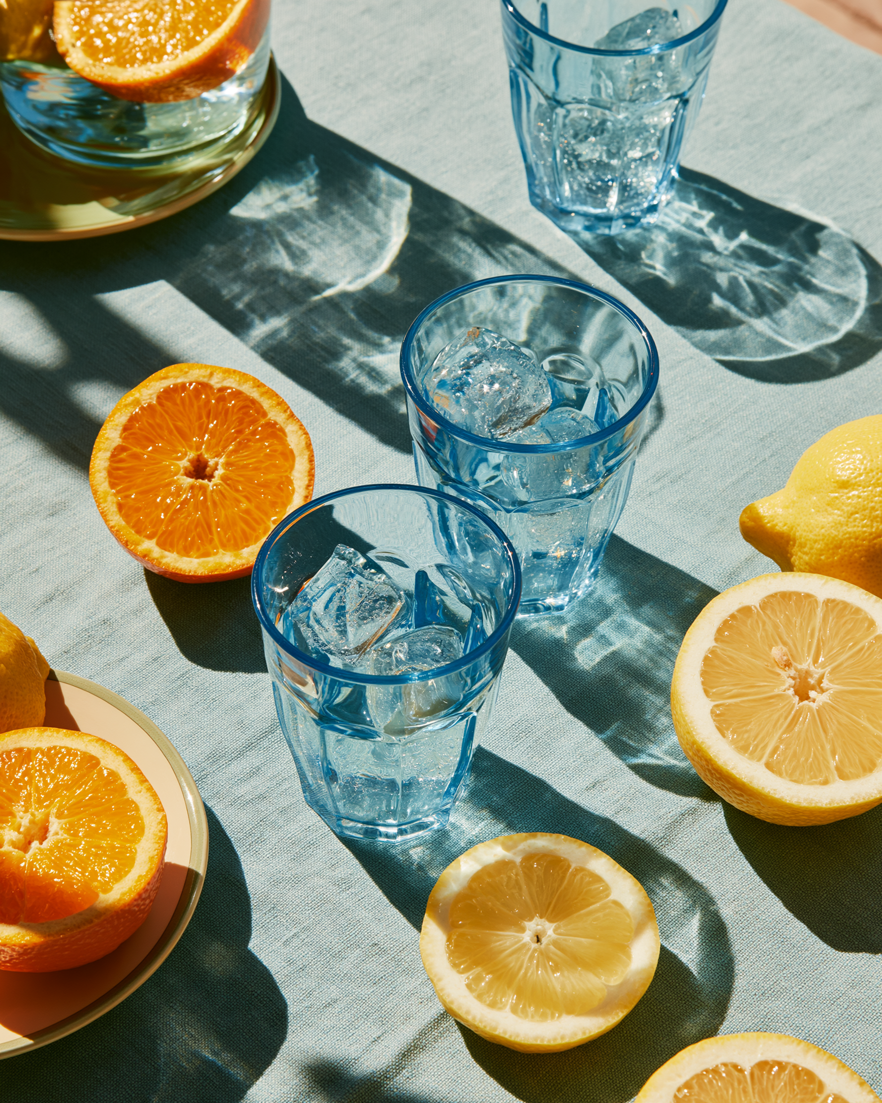 Blue glasses with ice and lemon slices on a gray surface with oranges and lemons.